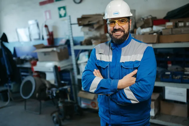 Smiling worker in blue uniform and hard hat standing in a factory setting in Russia. Formazione in azienda: obblighi, incentivi e piani formativi